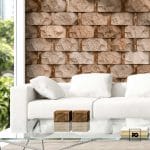 Fachaleta tipo piedra 30x45-cafe-foncer-plomeria garcia-2-ok | Plomería García Modern living room with a white sofa, glass coffee table, two small wooden boxes, and a beige stone accent wall.